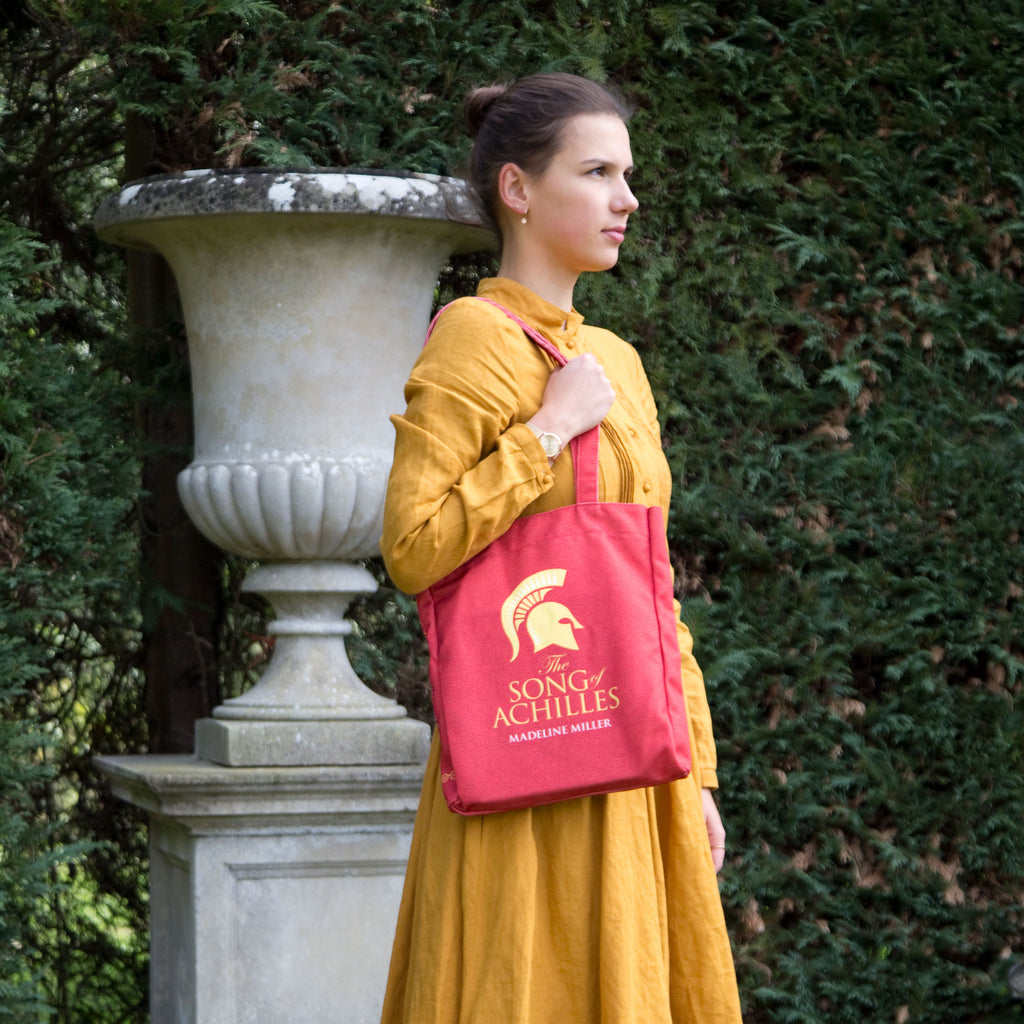 The Song of Achilles Red Tote Bag by Madeline Miller featuring Gold Trojan Helmet design, by Well Read Co. - Model Standing