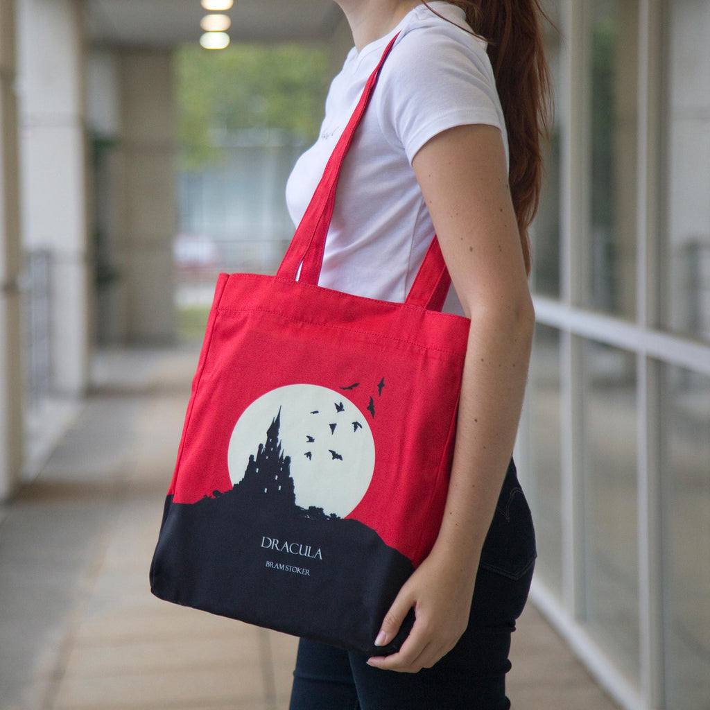 Dracula Red Tote Bag by Bram Stoker featuring Black Castle and Bats design, by Well Read Co. - Girl Standing