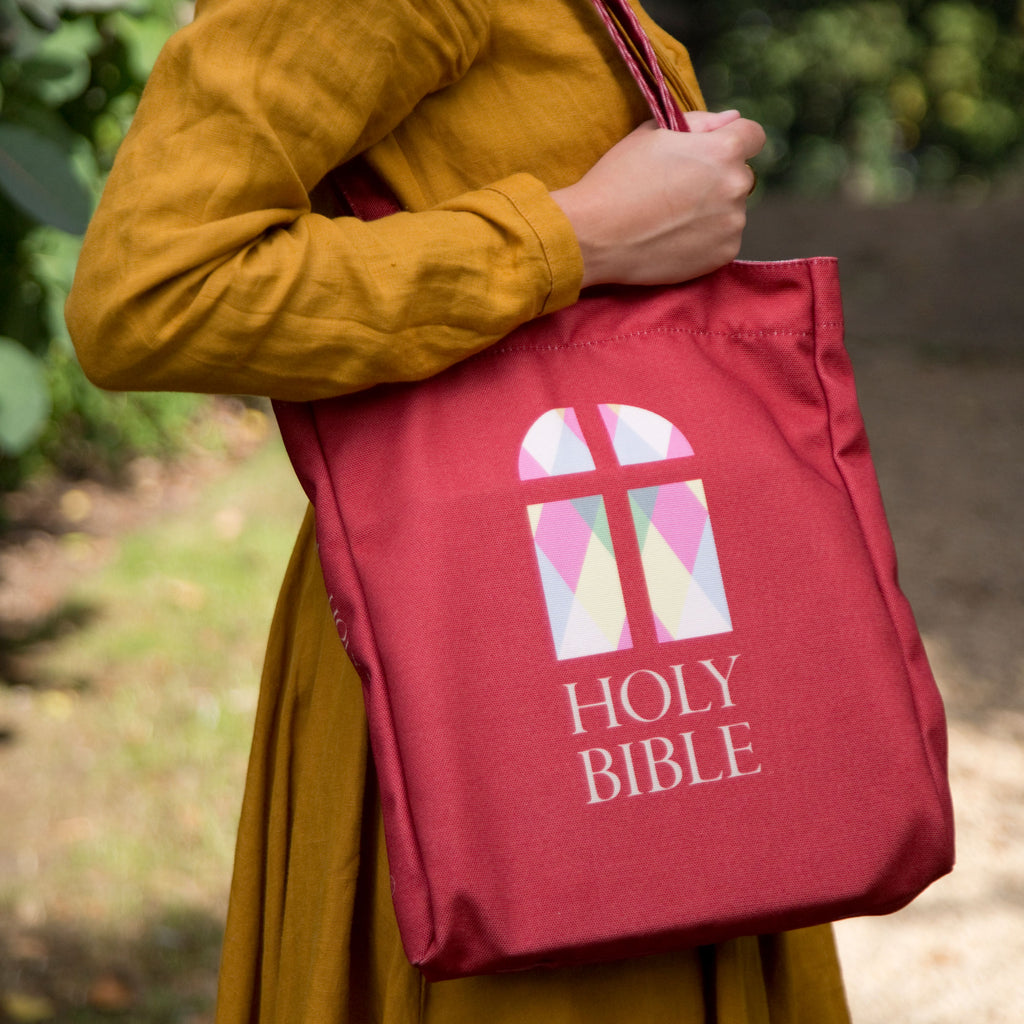 The Holy Bible Red Tote Bag by Well Read Co. featuring Stained-Glass Window design - Model Sitting with Bag